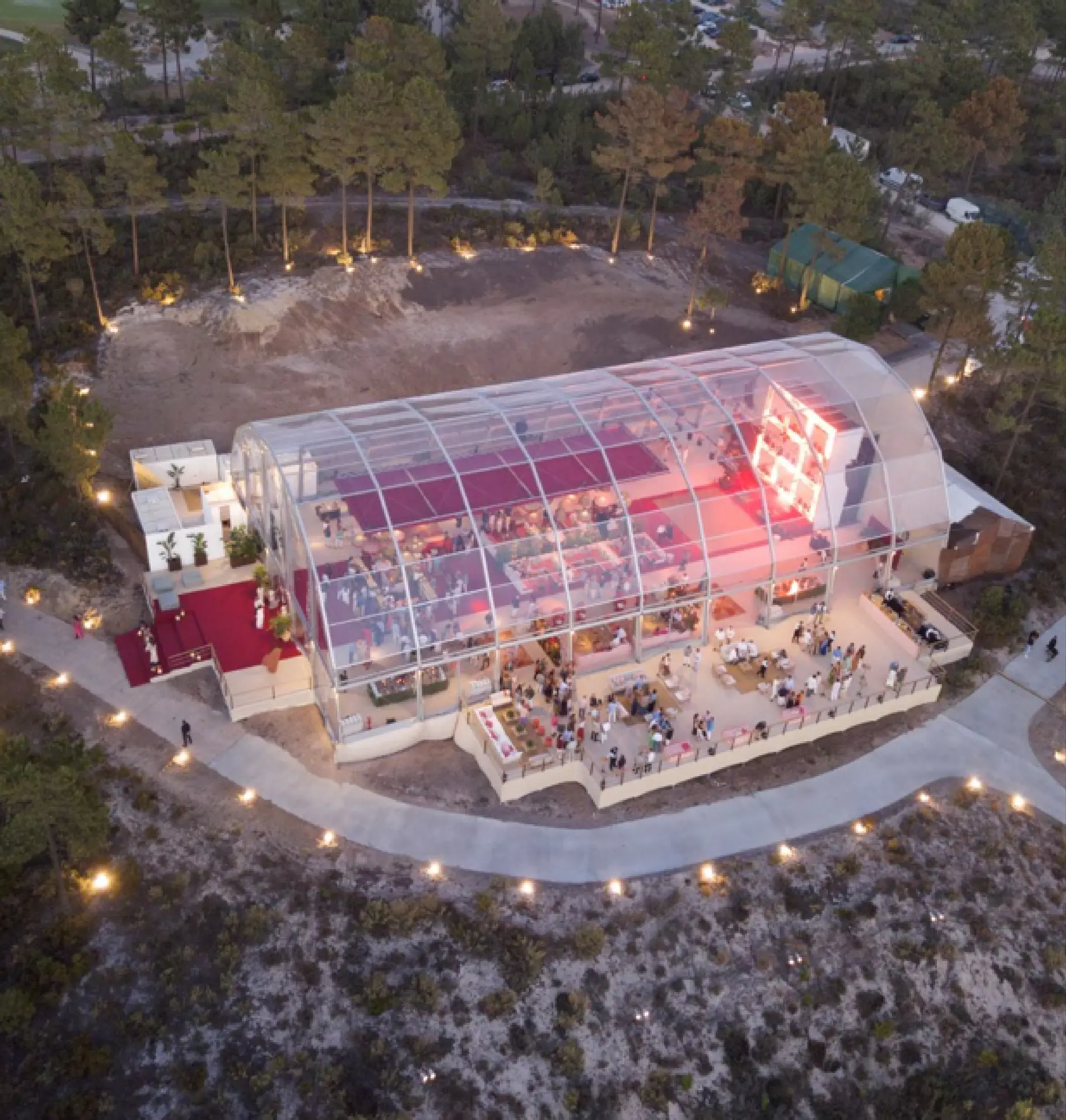 Vista aérea de uma tenda iglo transparente iluminada ao anoitecer, rodeada de luzes