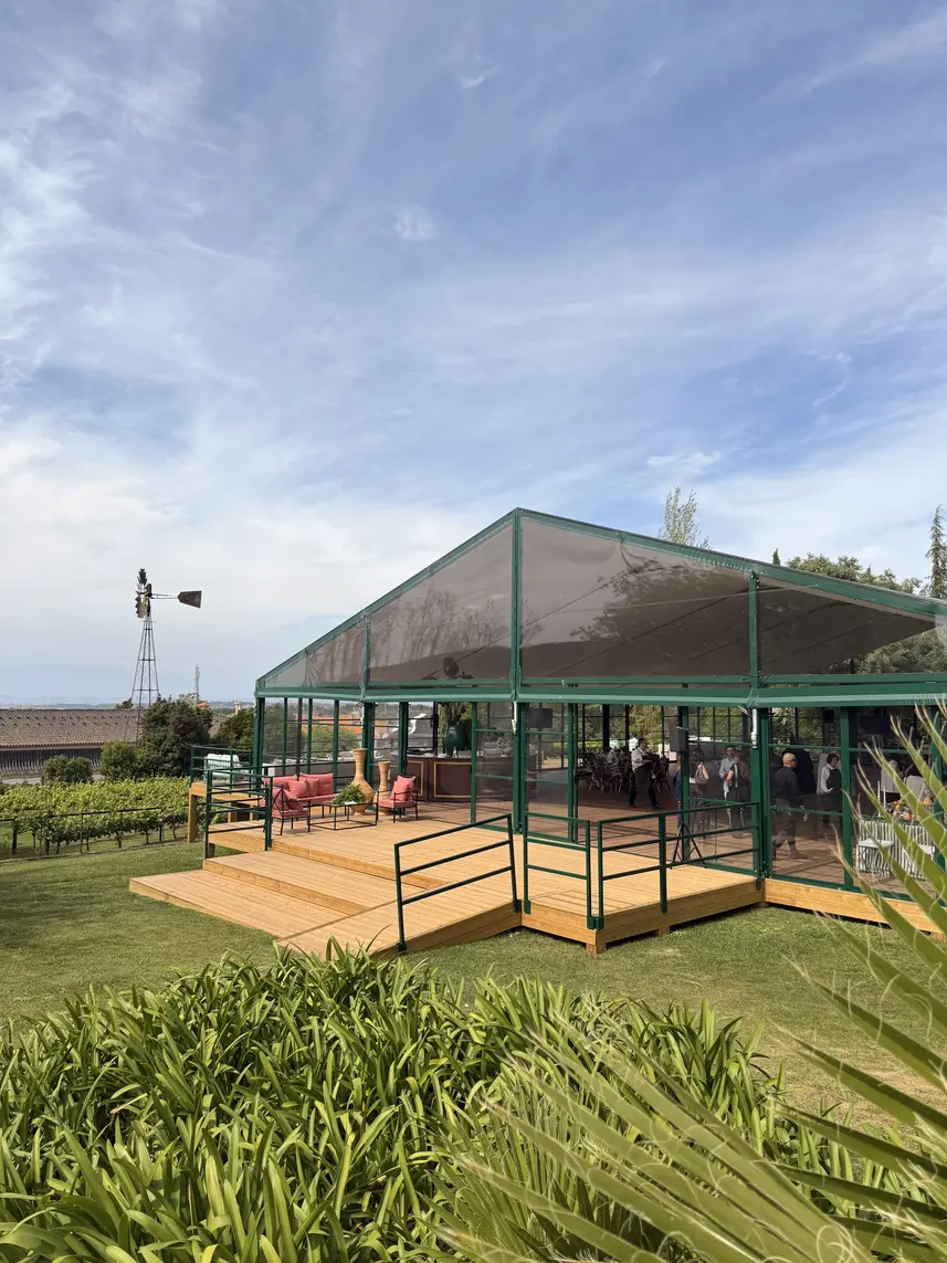 Tenda transparente de estrutura verde sobre um deck de madeira, nos jardins da José Maria da Fonseca