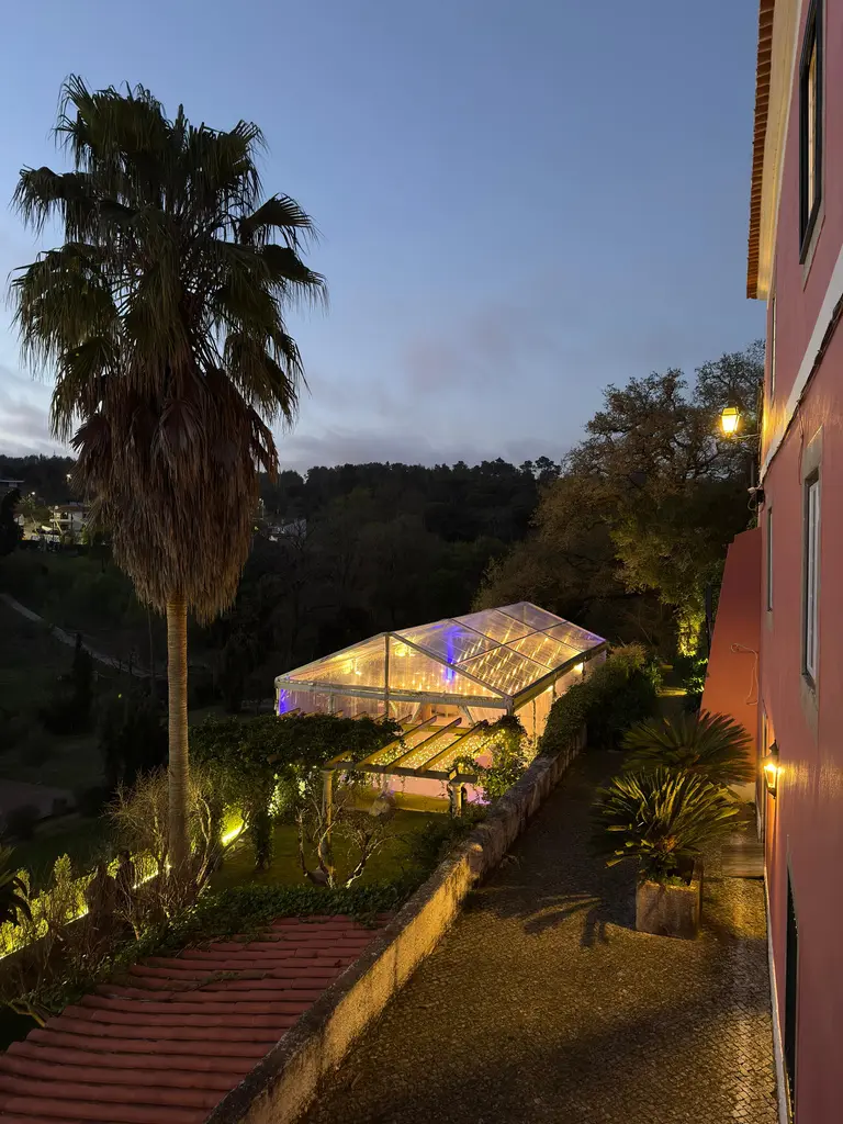 Tenda transparente iluminada ao anoitecer no jardim da Quinta de São Tadeu, entre palmeiras