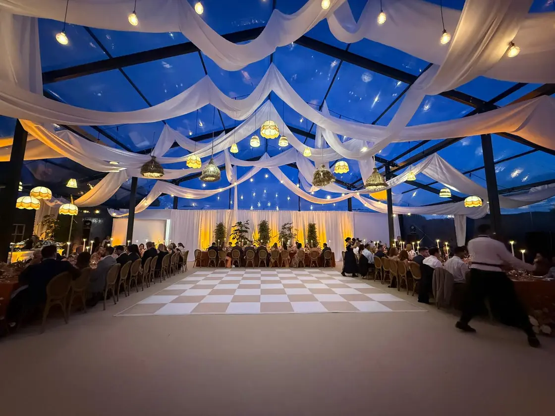 Interior de tenda à noite com tecido branco drapeado no tecto e pista de dança em xadrez