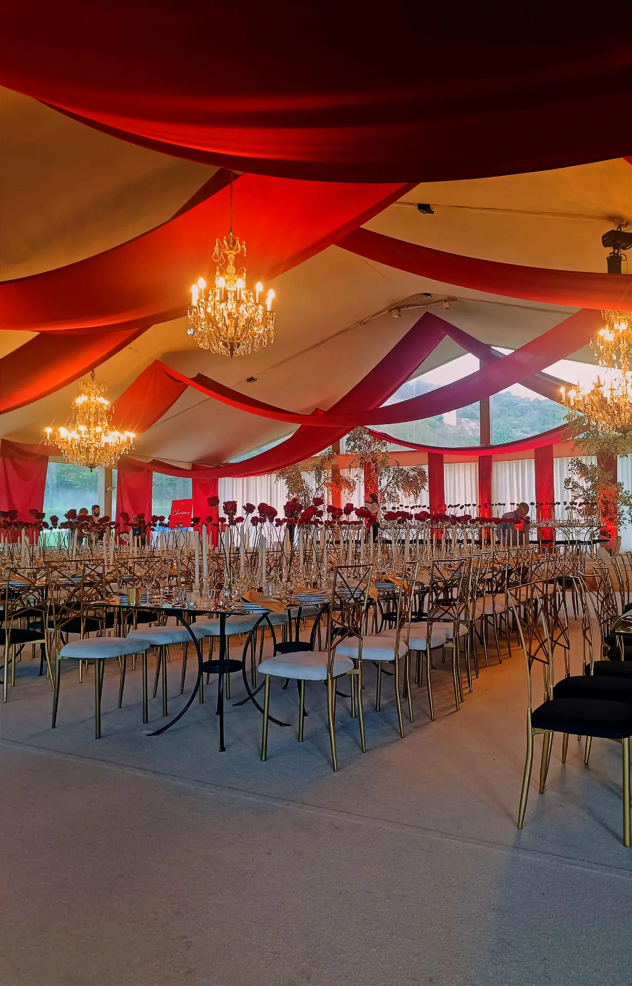 Interior de tenda com tecido vermelho drapeado no tecto e lustres de cristal