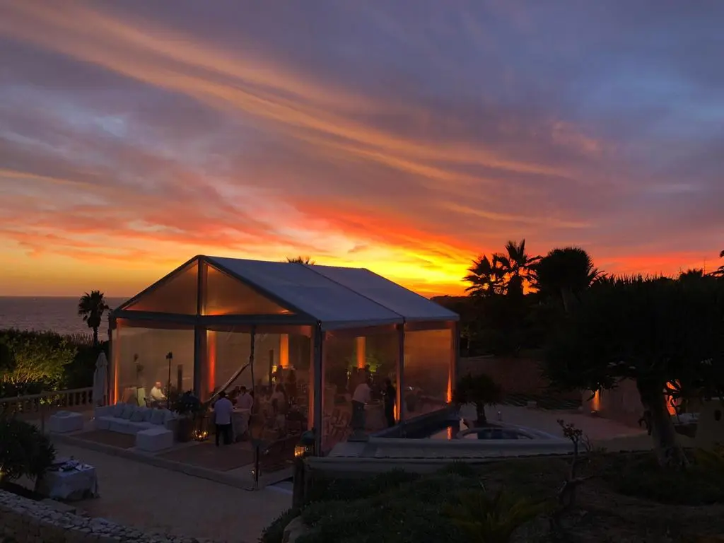 Tenda pequena ao pôr-do-sol, com o céu laranja por cima do mar